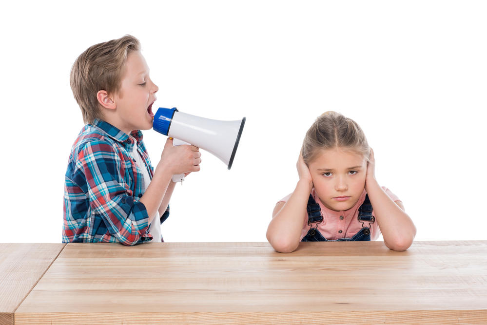 young boy with a megaphone shouting in the ear of a young girl trying to ignore him